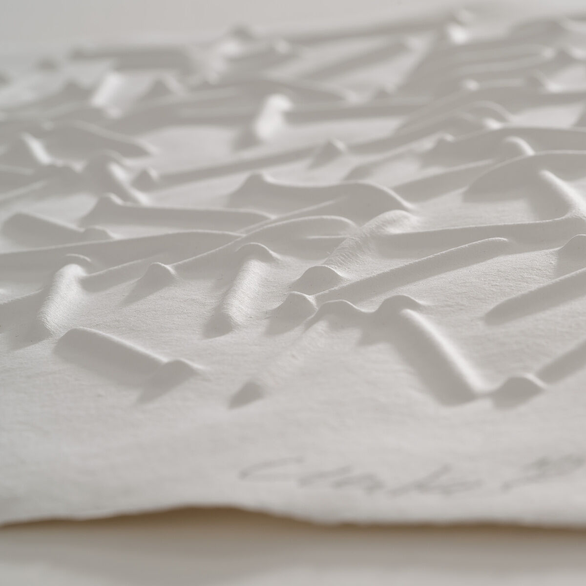 Das Bild zeigt eine weiße Prägedruck-Grafik von Günther Uecker, mit abstrakten, reliefartigen Mustern, die Schatten werfen. Es ist Teil der Benefizgrafiken für das Lilli Marx Haus in Düsseldorf.