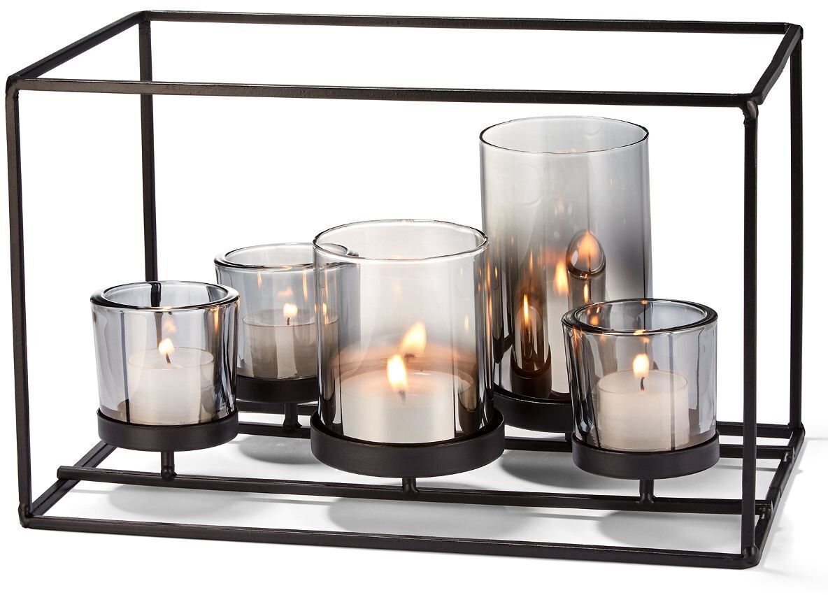 Ein moderner Kerzenhalter aus Metall- und Glaskonstruktion mit mehreren Kerzen unterschiedlicher Größe, die in einem rechteckigen, offenen Rahmen angeordnet sind. Schwarz, grau und weiß dominieren die Farbpalette.