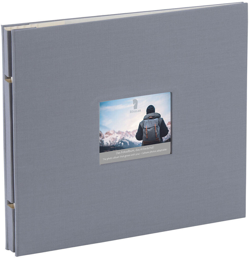 Ein graues Fotoalbum mit einem kleinen Fenster auf dem Cover, das ein Foto von einer Person mit einem Rucksack in einer Berglandschaft zeigt.