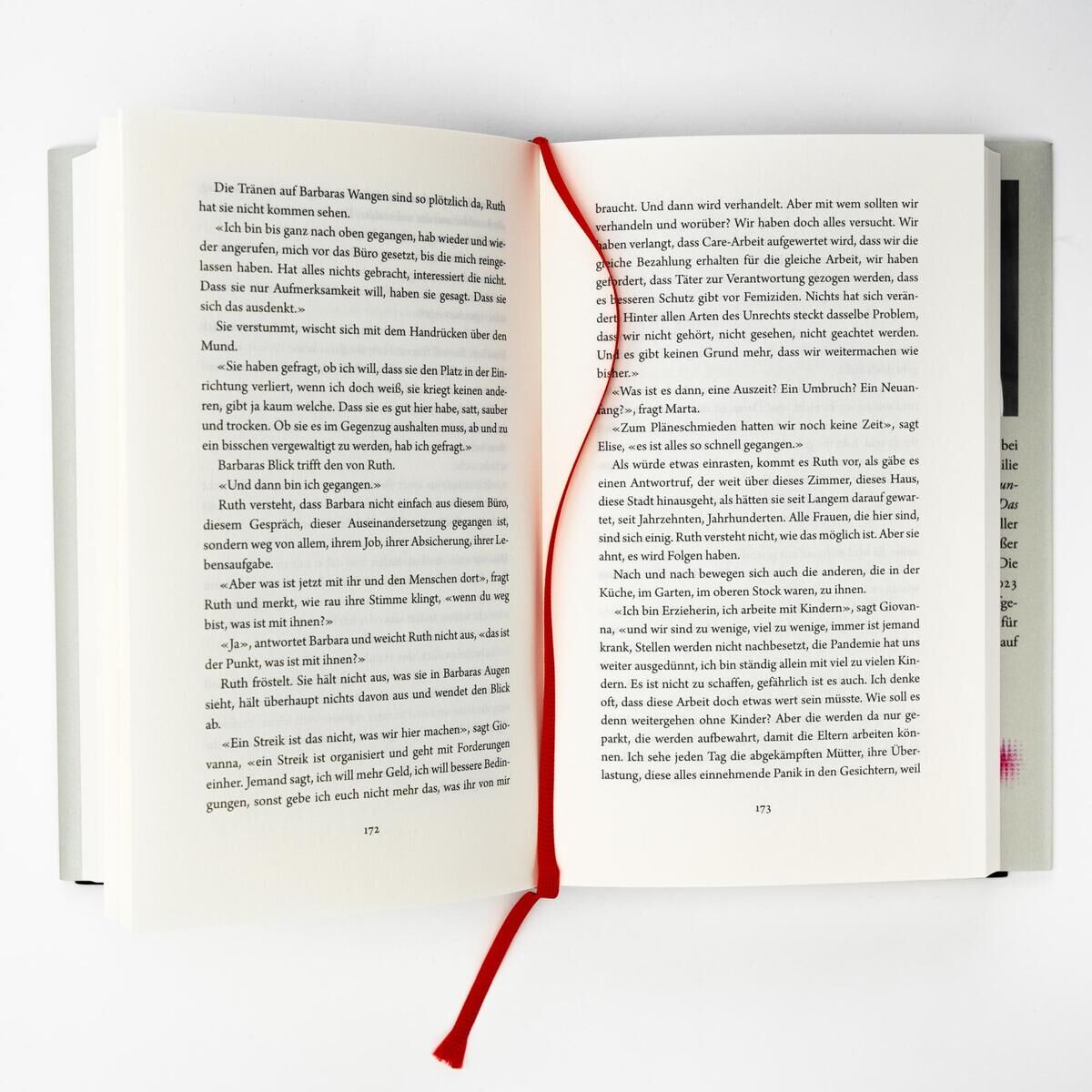 Ein geöffnetes Buch mit schwarzem Text auf weißen Seiten. Ein rotes Lesezeichen liegt zwischen den Seiten.