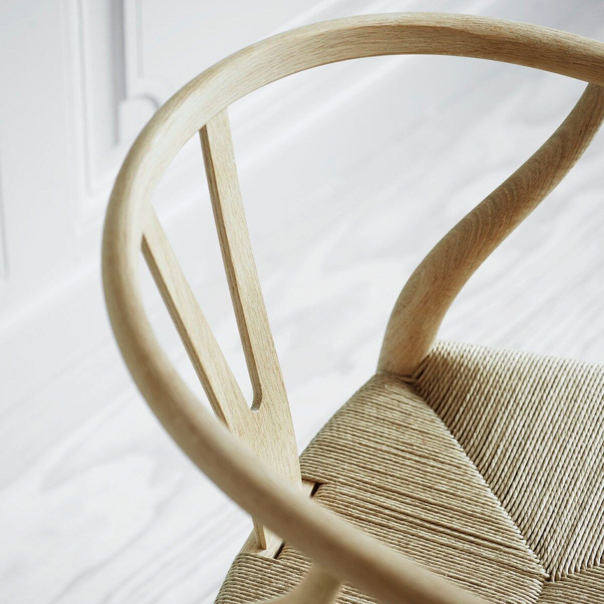 Nahaufnahme eines Wishbone Chair »CH24« von Carl Hansen & Søn mit hellem Holzgestell und geflochtenem Sitz. Der Stuhl ist minimalistisch gestaltet und repräsentiert skandinavisches Design.