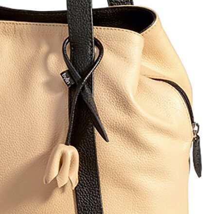 Detailansicht eines cremefarbenen Shoppers aus Leder der Marke Ars mundi. Die Tasche besitzt schwarze Tragegriffe und eine schwarze Zierquaste mit cremefarbenem Anhänger in Tulpenform. Sichtbar ist eine dezente Narbenstruktur des Leders sowie ein seitlicher Reißverschluss.