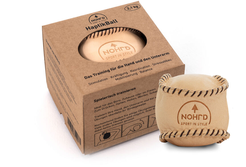 Ein HaptikBall »Natur« aus Holz ist neben einer kleinen Verpackung abgebildet. Die Verpackung zeigt das Logo und verschiedene Informationen über den HaptikBall. Der Ball ist beige mit schwarzen farbigen Verzierungen.