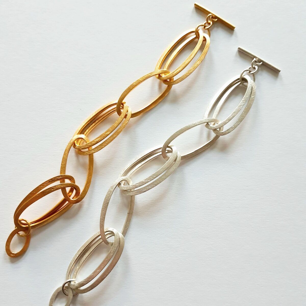 Zwei HML-Armbänder »GRACE« in Gold- und Silberfarben mit länglichen, ovalen Gliedern auf weißem Hintergrund.