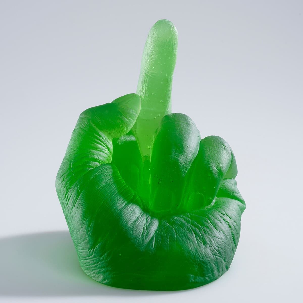 Eine grüne Glaskulptur einer hochgehaltenen Mittelhand vor einem grauen Hintergrund, geschaffen von Ai Weiwei.