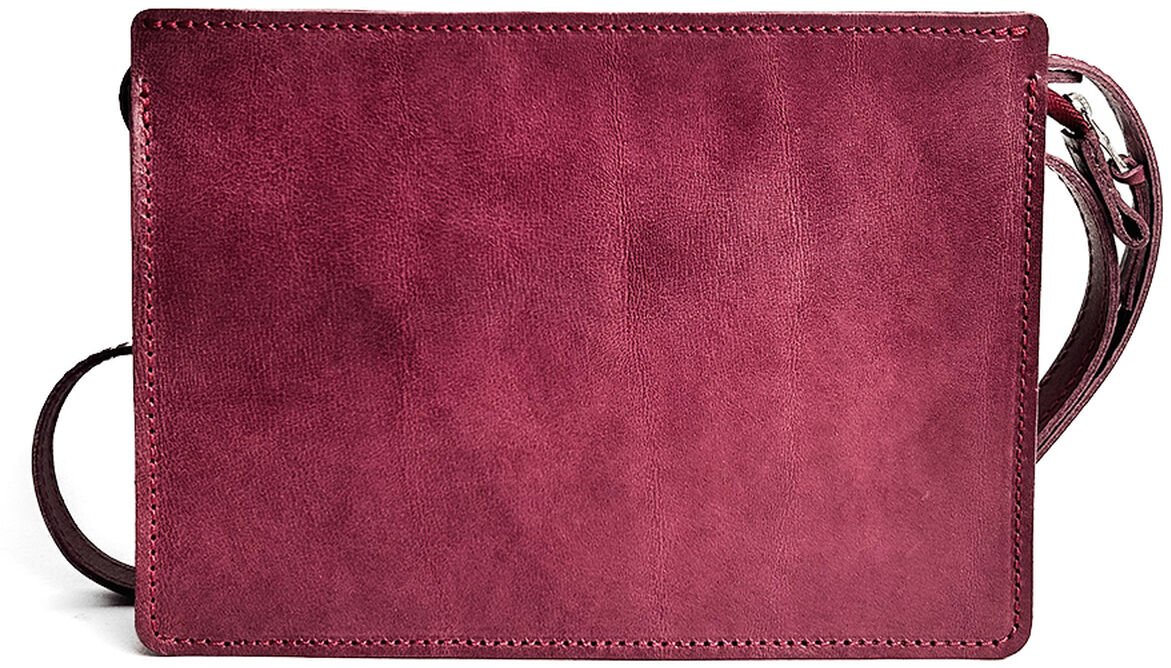 Abgebildet ist eine rechteckige Umhängetasche aus bordeauxrotem Kernleder mit schlichtem, zeitlosem Design und verstellbarem Riemen. Die Tasche liegt auf hellem Untergrund.