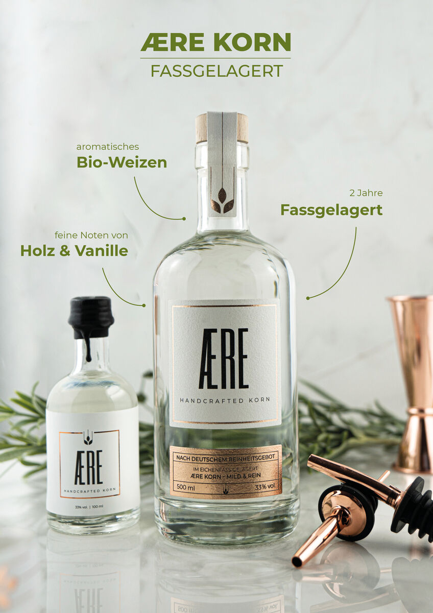 Zwei Flaschen AERE Korn aus Bio-Weizen, eine große und eine kleine, auf einer Marmor-Oberfläche mit verschiedenen Barzubehörteilen.