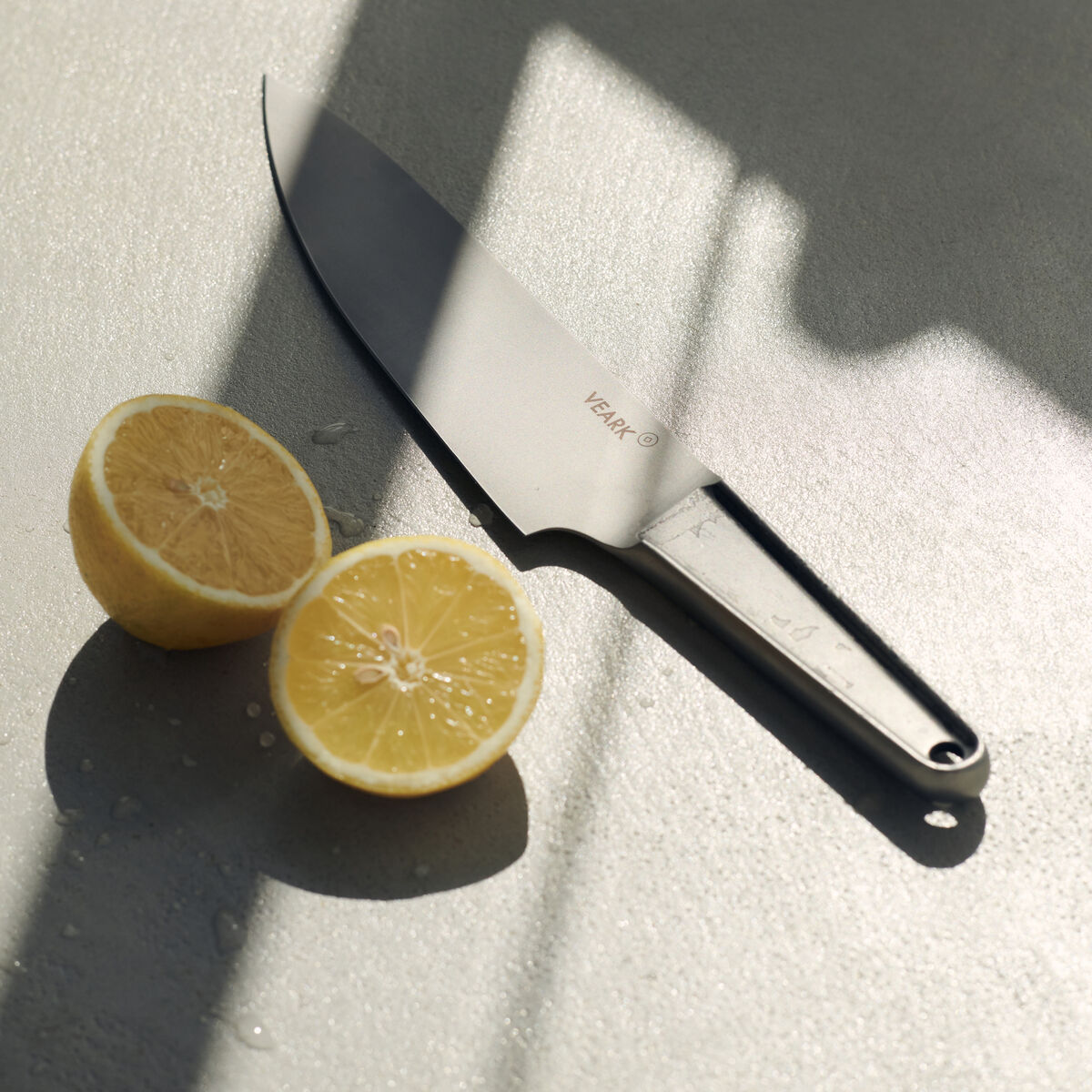 Ein hochwertiges Küchenmesser aus rostfreiem Stahl liegt auf einer grauen Oberfläche neben zwei Hälften einer Zitrone.