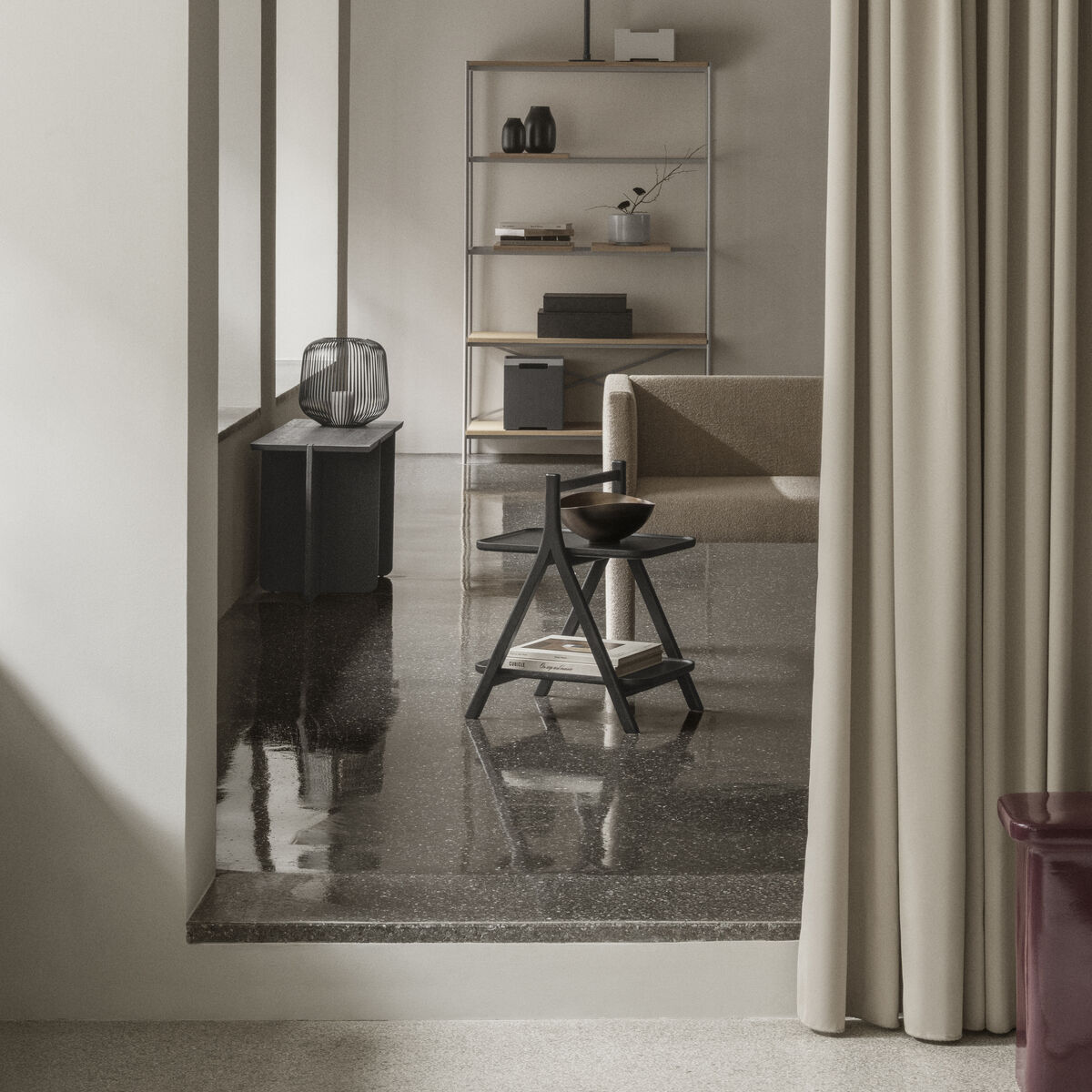 Modern eingerichtetes Wohnzimmer mit Beistelltisch »ETA« von blomus aus massiver Eiche in Naturfarbe. Der stabile A-Rahmen wirkt schwebend, mit sanft abgerundeten Kanten und zwei Ebenen. Im Hintergrund ein Sofa, Regal und weitere Deko, dezente Farbpalette, ruhiges Ambiente.