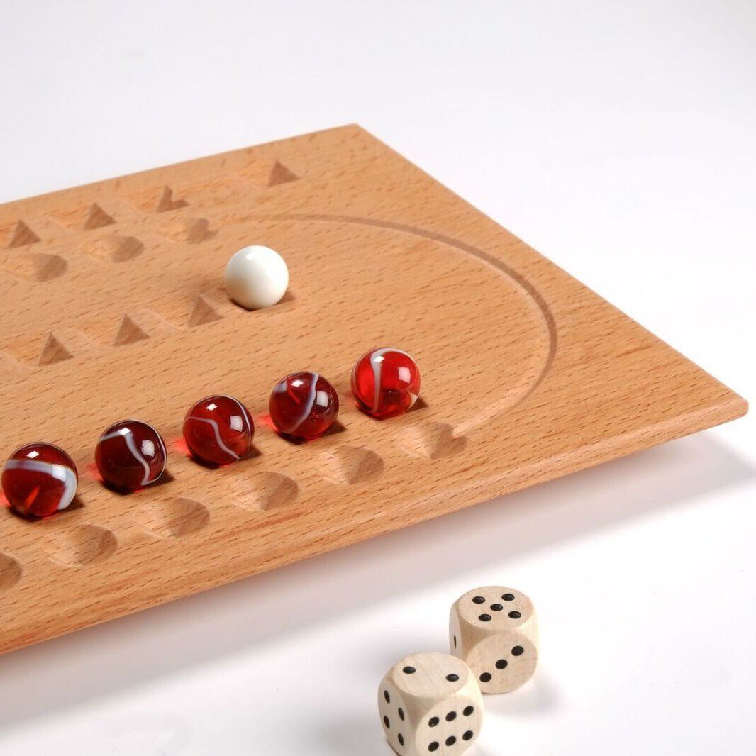 Ein Brettspiel aus Holz namens Samsara mit roten und weißen Murmeln. Das Spielbrett hat Vertiefungen und ist auf einem weißen Hintergrund zu sehen. Zwei Würfel sind im Vordergrund platziert.