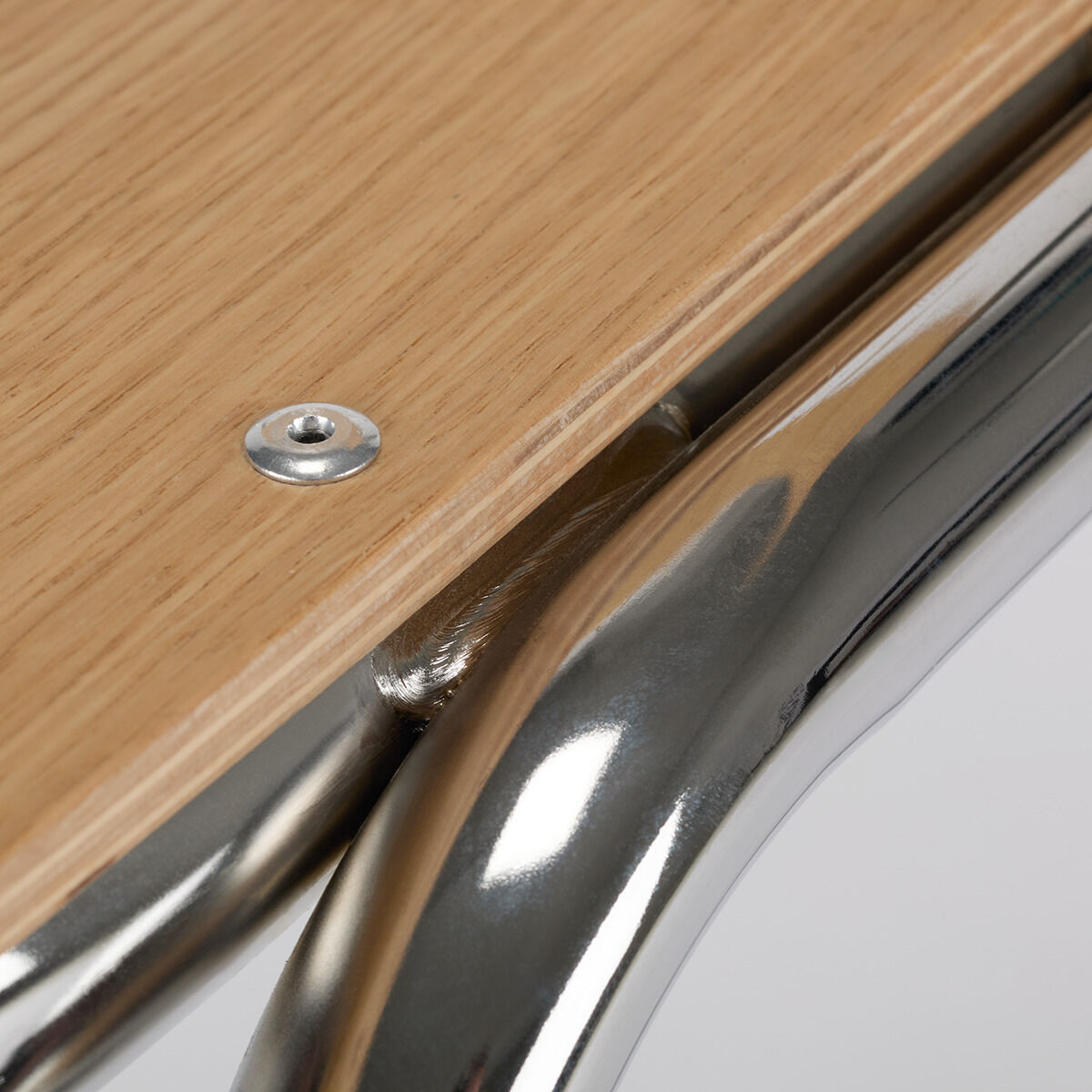 Detailansicht eines modernen Stuhls mit einer glatten Holzsitzfläche und glänzenden, metallischen Beinen.