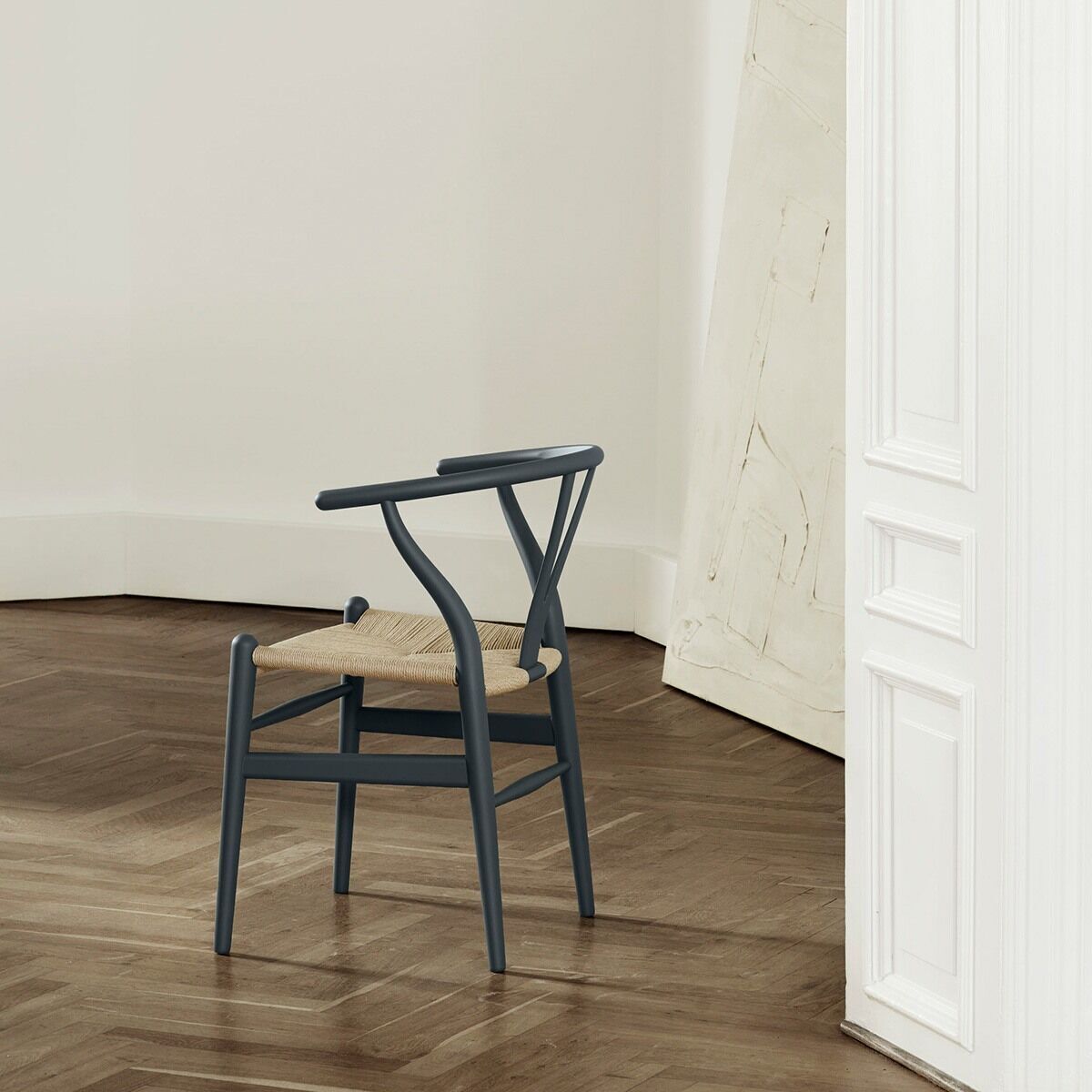 Moderner Stuhl CH24 Soft von Carl Hansen in grau mit naturfarbenem Sitz, präsentiert in einem minimalistisch eingerichteten Raum mit Holzboden.