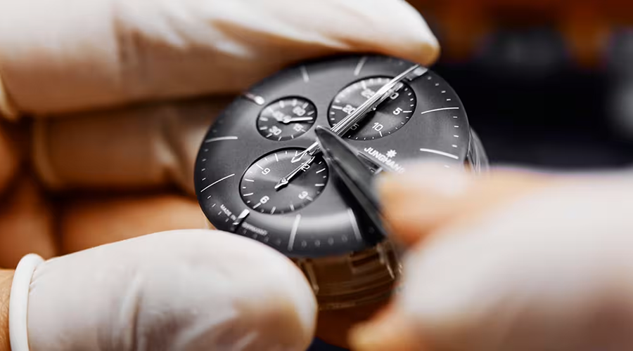 Nahaufnahme eines Uhrmacherhands, der mit einer Pinzette an einem schwarzen Zifferblatt einer Armbanduhr arbeitet