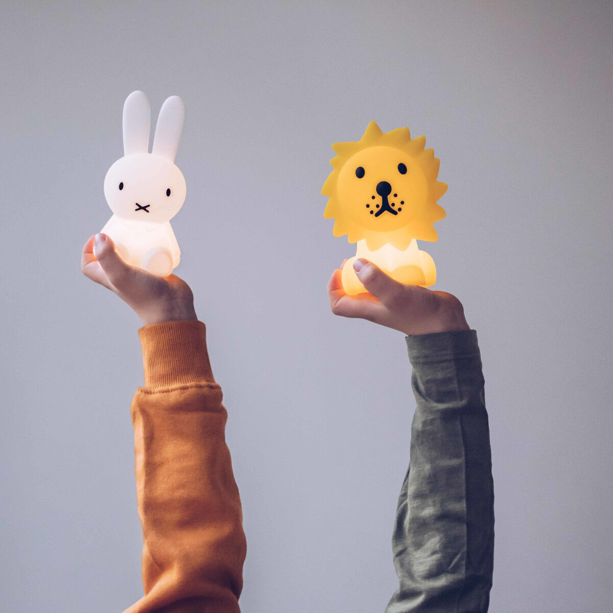 Zwei Nachtlichter in Form von Tieren werden in Händen gehalten. Links ist die weiße Miffy-Kaninchen-Lampe und rechts eine gelbe Löwen-Lampe. Perfekt für Kinderzimmer und als beruhigendes Nachtlicht.
