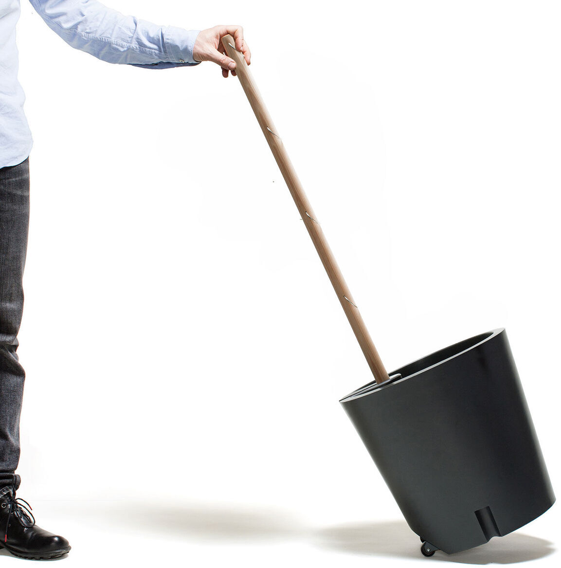 Ein mobiler Pflanzkübel mit ergonomischem Griff wird von einer Person in Jeans und blauem Hemd gehalten. Der Kübel hat Rollen für einfache Bewegung.