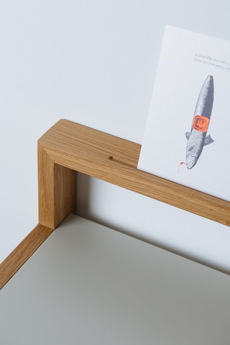 Stehpult 'buckowski' aus Holz mit einer minimalistischen und ergonomischen Gestaltung. Ein moderner, multifunktionaler Arbeitsplatz, der sich gut für Büros oder Heimarbeitsplätze eignet. Auf dem Stehpult steht ein Buch mit einem Fisch und roten Details auf dem Cover.