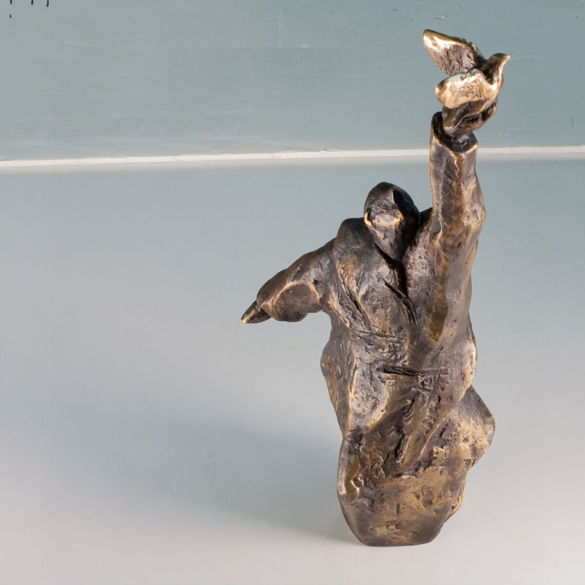 Bronzefarbene Skulptur von Christoph Fischer mit dem Titel 'Der Gedanke', die eine abstrahierte menschliche Figur mit erhobenem Arm darstellt.
