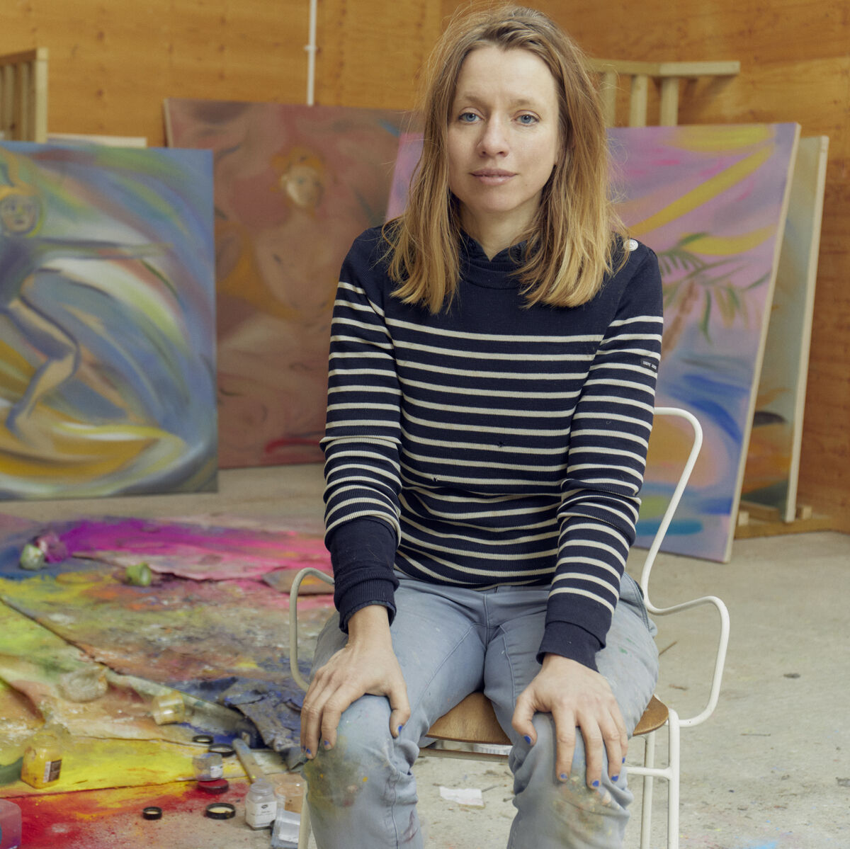 Ein gerahmtes Kunstwerk der ZEIT-Sonderedition Lithografie »DG 75B«, 2024, Nr. 4. Im Hintergrund eine Künstlerin in einem Atelier mit diversen Kunstwerken und farbigen Materialien auf dem Boden. Das Bild ist farbenfroh und abstrakt und zeigt verschiedene künstlerische Elemente.