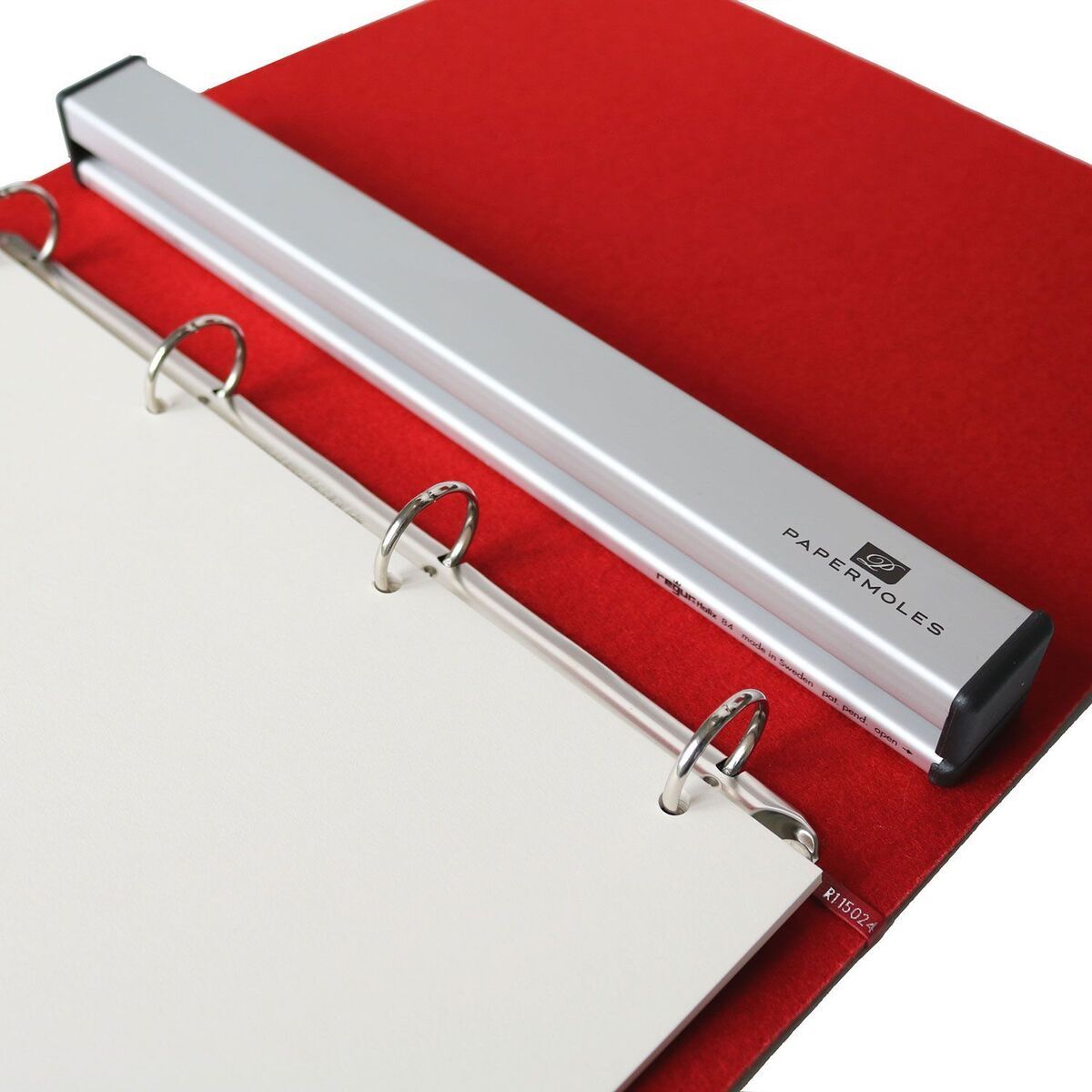 Ein metallischer Locher für PortRing A4, der auf einem roten Aktenordner liegt. Der Locher hat eine schlanke, längliche Form und ist aus Silber und Schwarz gefertigt. Es ist ein effizientes und praktisches Werkzeug für die Büroorganisation.