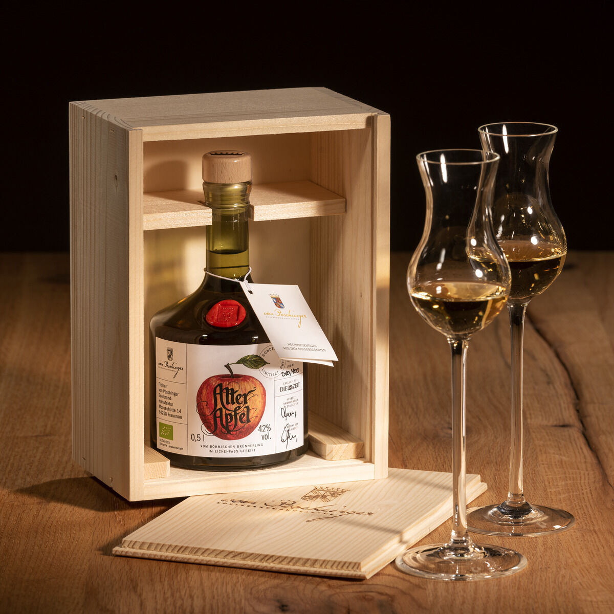 Eine Flasche ZEIT-Sonderedition »Alter Apfel« Edelbrand in einer Holzkiste präsentiert, mit zwei edlen Schnapsgläsern auf einem Holzuntersetzer.