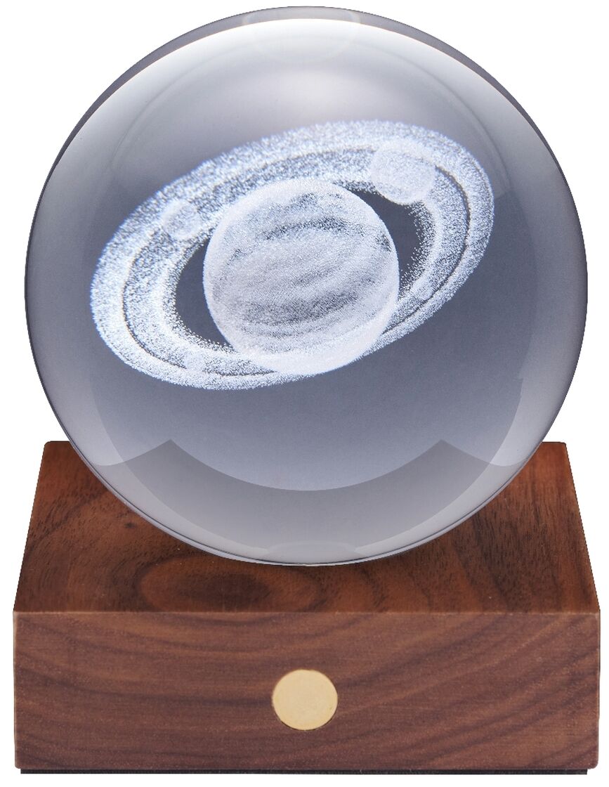 Eine dekorative Lampe namens »Amber Light« mit einer durchsichtigen Kugel auf einem rechteckigen Sockel aus dunklem Holz. In der Kugel ist eine detailreiche Darstellung des Planeten Saturn eingraviert. Die Lampe steht vor weißem Hintergrund.