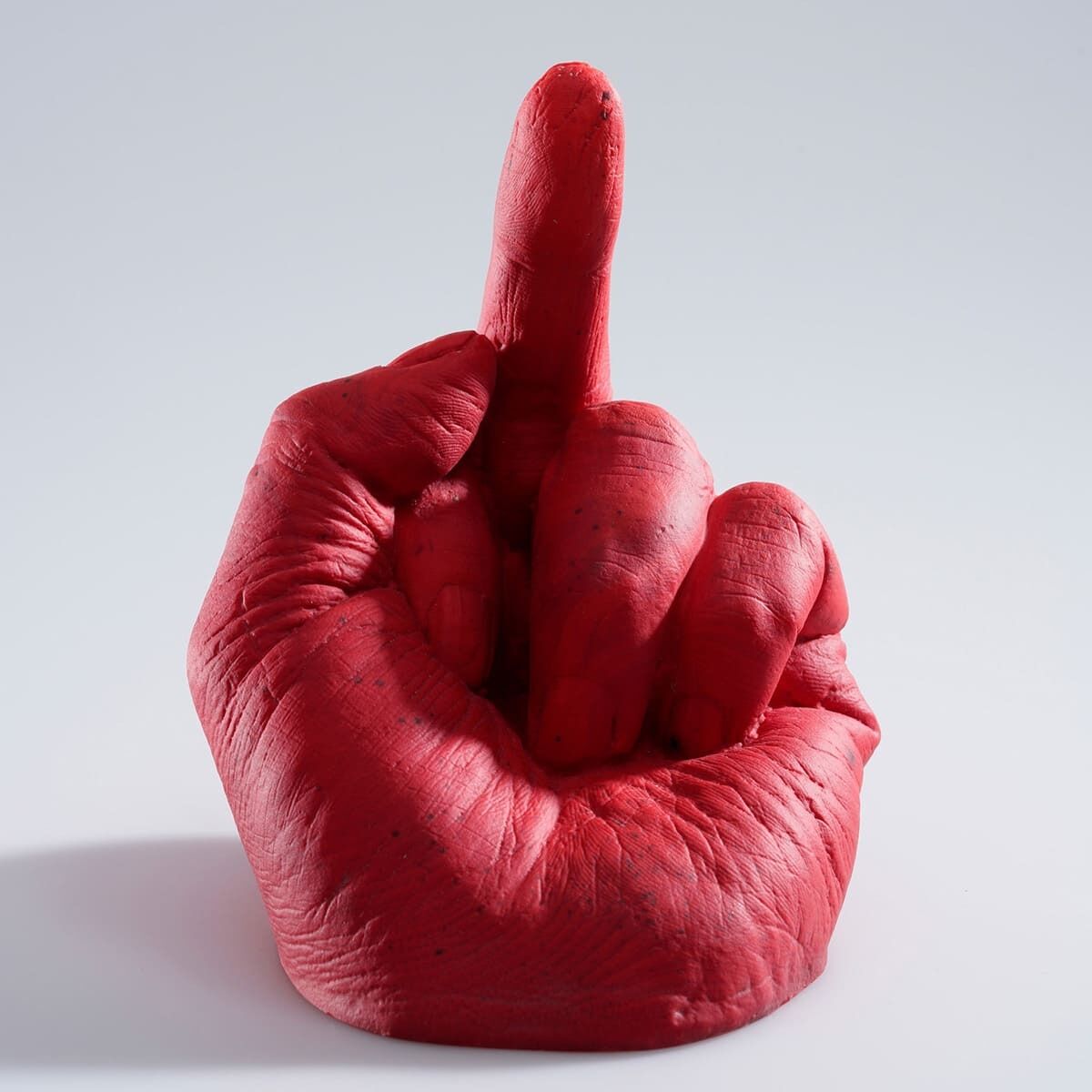 Die Skulptur »Study of Perspective in Glass« von Ai Weiwei zeigt eine rote Hand, die den Mittelfinger aufrecht zeigt, vor einem hellen Hintergrund. Die Skulptur kombiniert Elemente der modernen und politischen Kunst, wobei sie eine starke Aussage trifft.