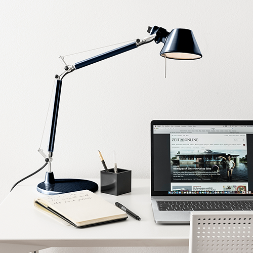 Schwarze verstellbare Schreibtischlampe neben offenem Laptop und Notizbuch auf weißem Tisch