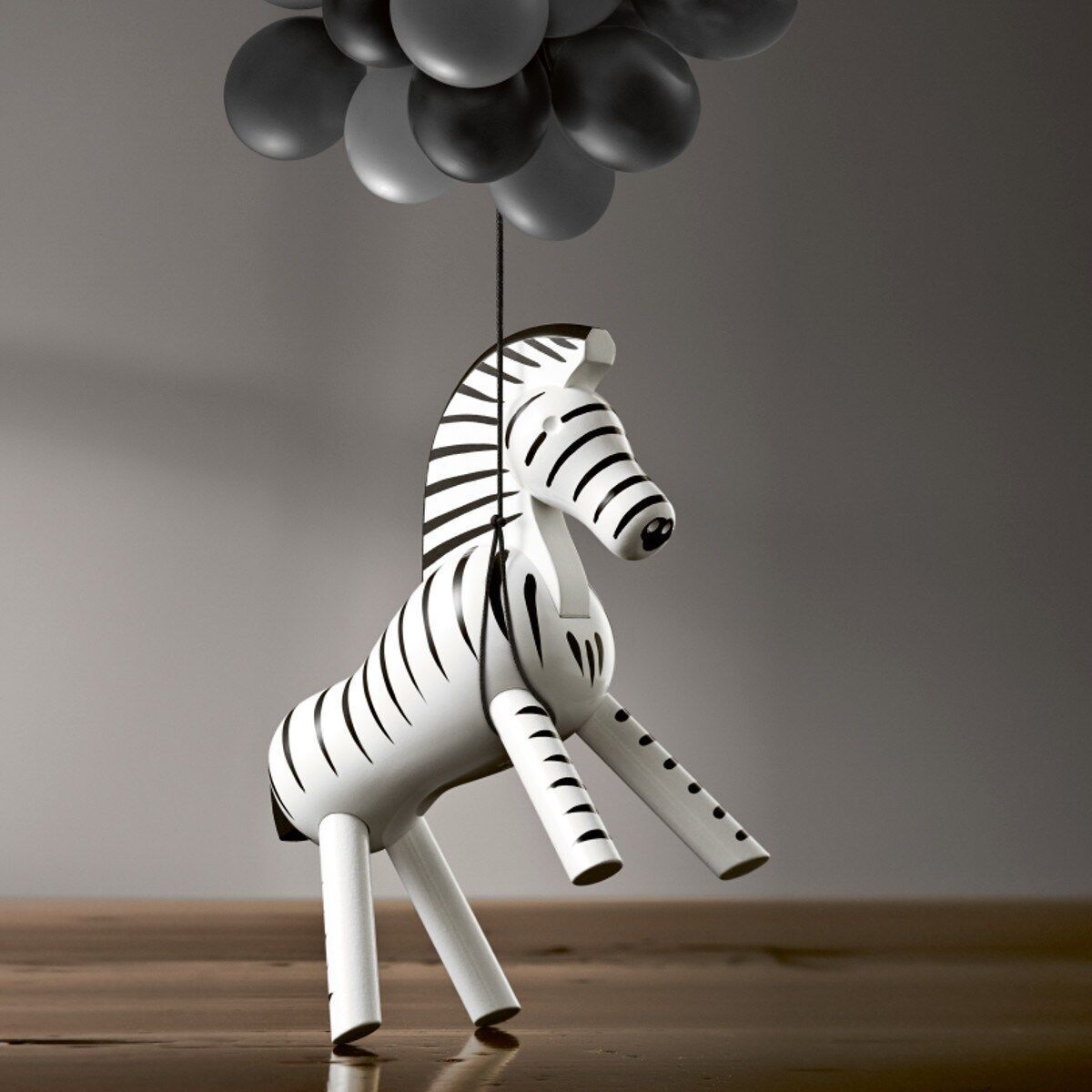 Holzfigur eines Zebras von Kay Bojesen, elegant gestaltet mit traditionellen schwarzen und weißen Streifen, ausgestellt auf einem Holzuntergrund mit grauen Ballons im Hintergrund.