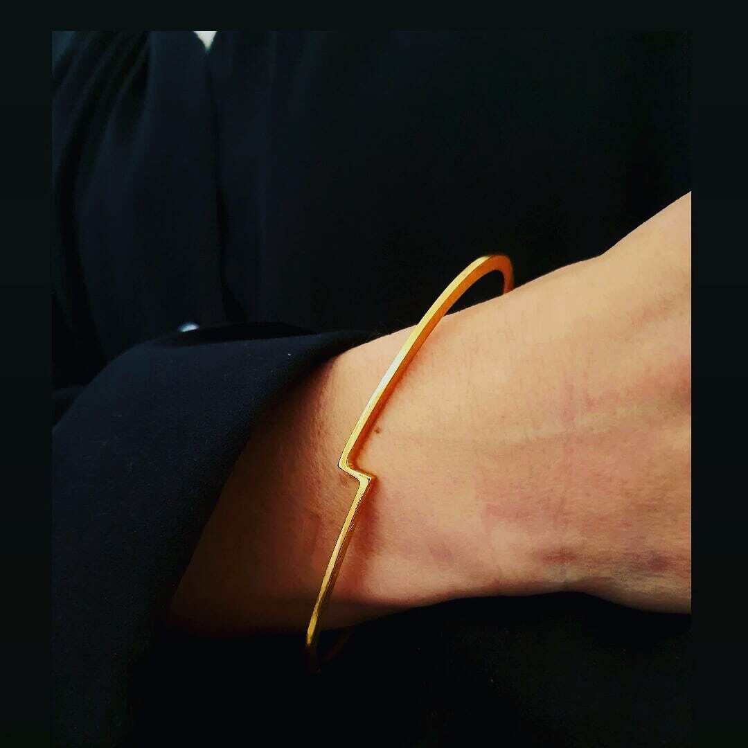 Ein eleganter, minimalistischer goldener Armreif am Handgelenk einer Person, die schwarze Kleidung trägt.