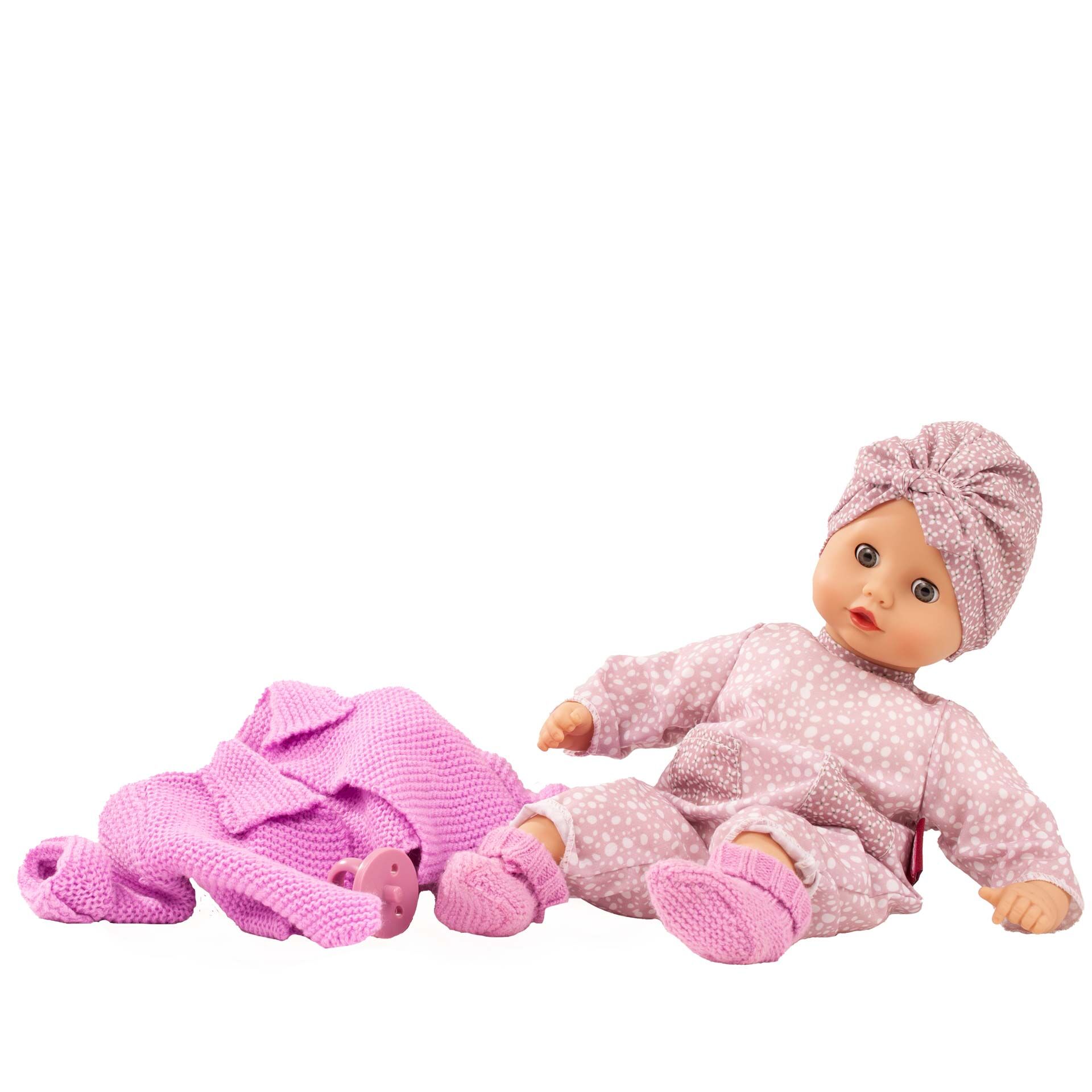Abgebildet ist eine weiche Babypuppe namens 'Muffin Baby Soft Mood' mit rosa gemustertem Strampelanzug und passender Kopfbedeckung, daneben liegen zusätzliche rosa Puppenkleidung und Accessoires. Die Puppe ist auf weißem Hintergrund platziert.