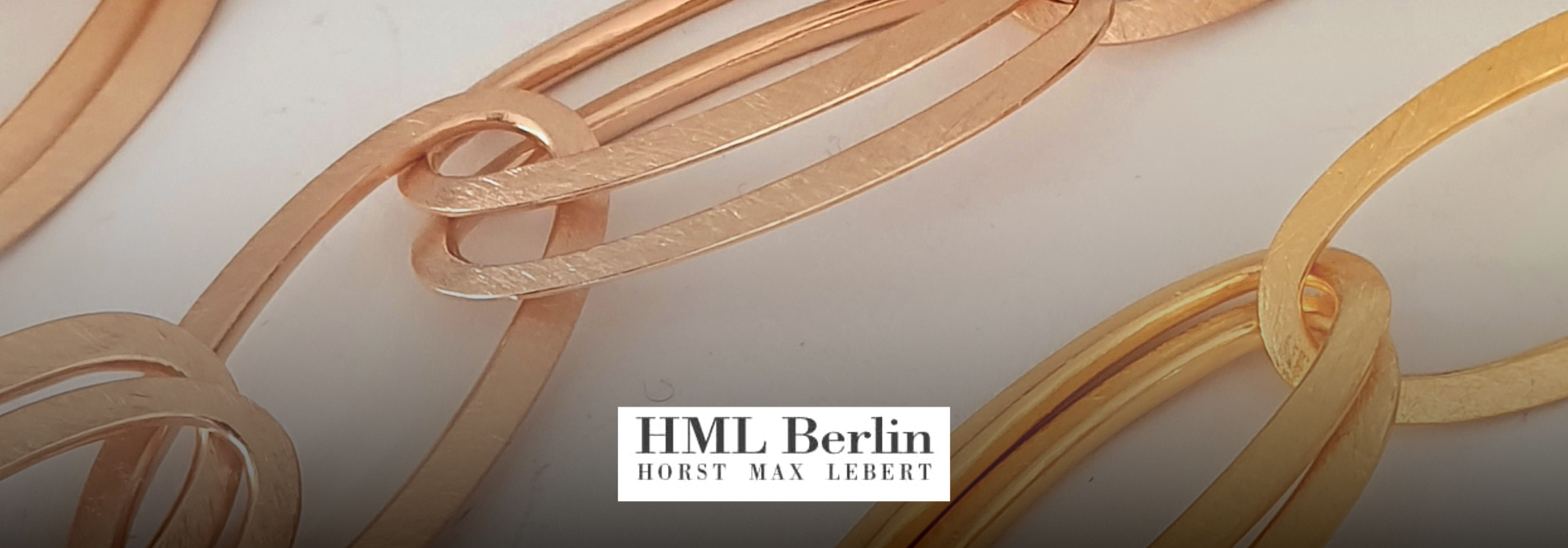 Goldfarbene, überlappende Metallringe mit dem Schriftzug 'HML Berlin HORST MAX LEBERT' in der Mitte