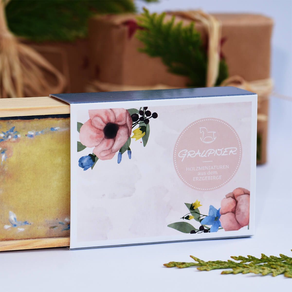 Ein Glückwunschkästchen mit der Aufschrift 'Brautpaar' in elegantem Design, verziert mit einem floralen Muster. Das Kästchen steht auf einem Tisch, im Hintergrund ist verschwommen Weihnachtsdekoration zu sehen.