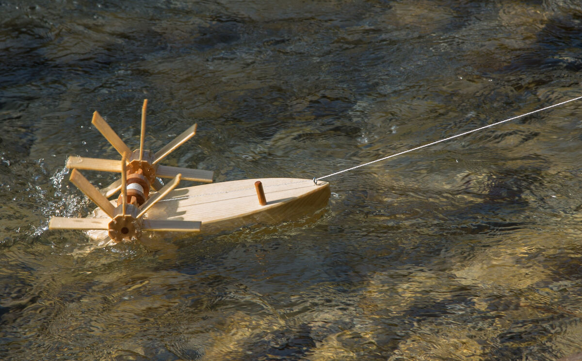 Bausatz »Forelle« zum Experimentieren: Ein hölzernes Modell eines Wasserrads und Boots schwimmt auf einem fließenden Gewässer.