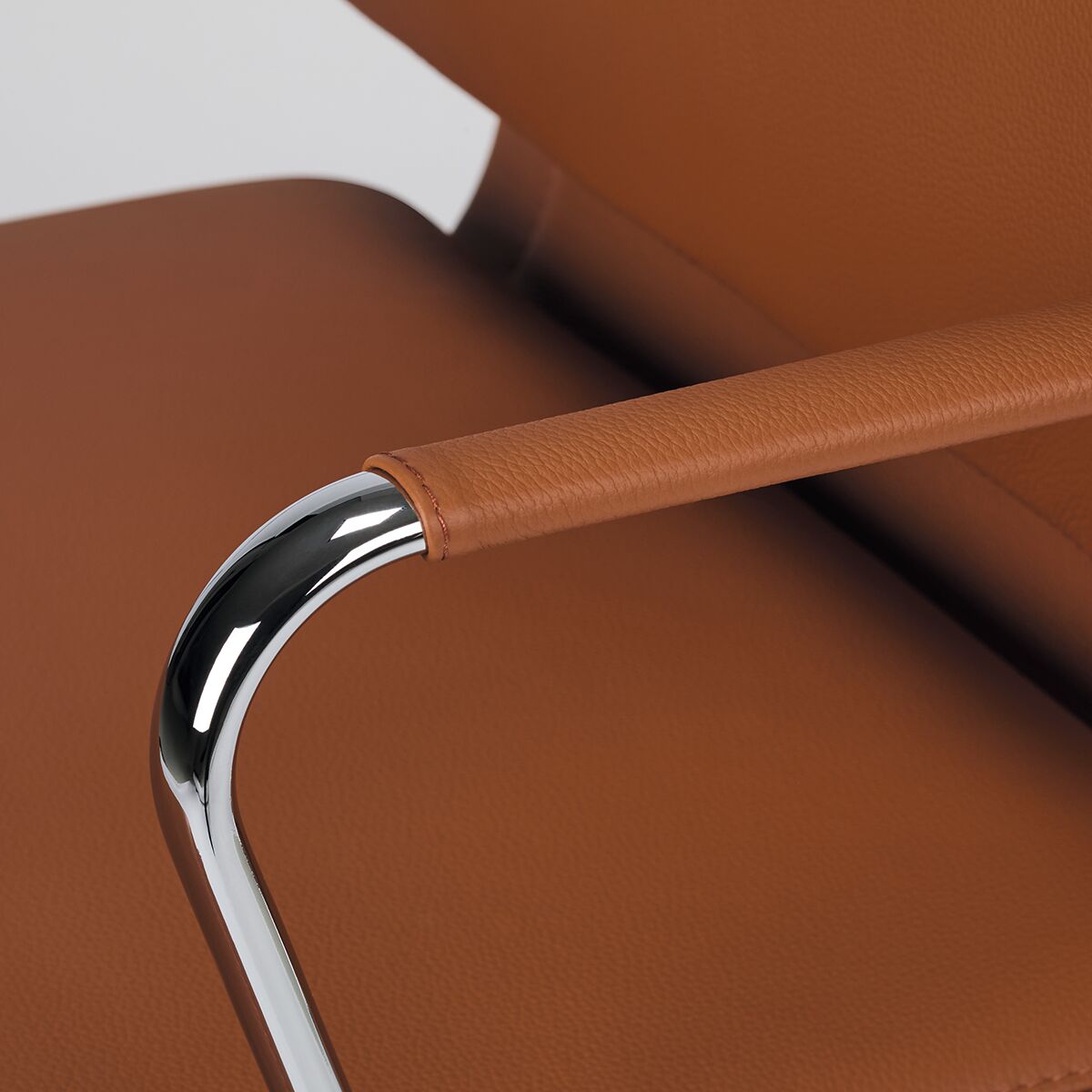 Ein Vitra Soft Pad Bürostuhl »EA217« mit braunem Lederbezug und verchromten Armlehnen im modernen Design.