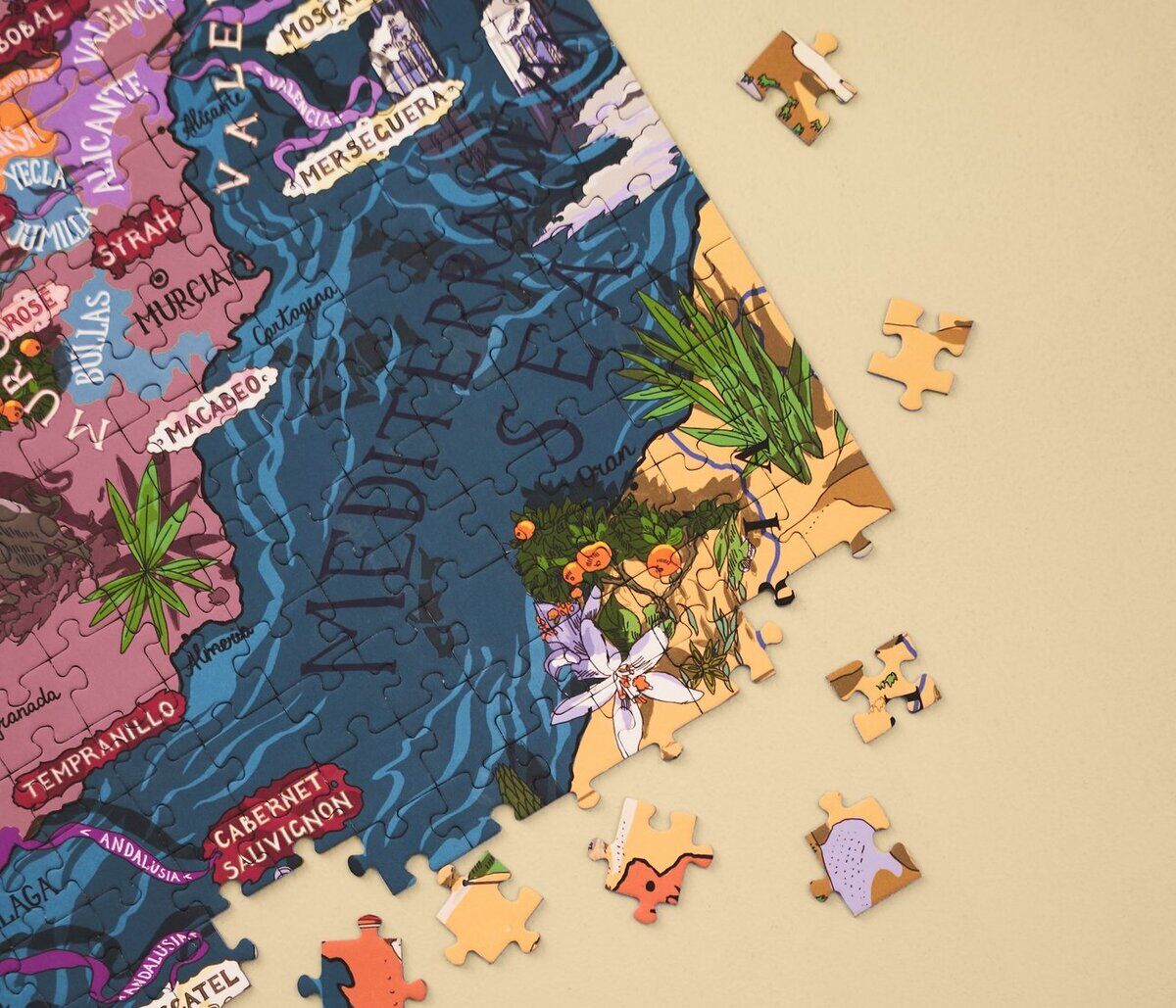 Ein Wein-Puzzle mit einer farbenfrohen Landkarte von Spanien, auf der verschiedene Weinregionen markiert sind. Puzzleteile liegen um das teilweise fertige Puzzle verstreut.