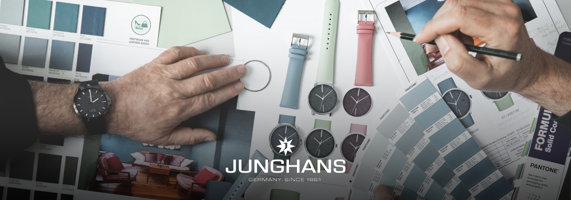 Zwei Hände arbeiten mit Farbmustern, Uhrenarmbändern und Junghans-Uhren auf einem Tisch, umgeben von Designmaterialien und Pantone-Farbkarten.
