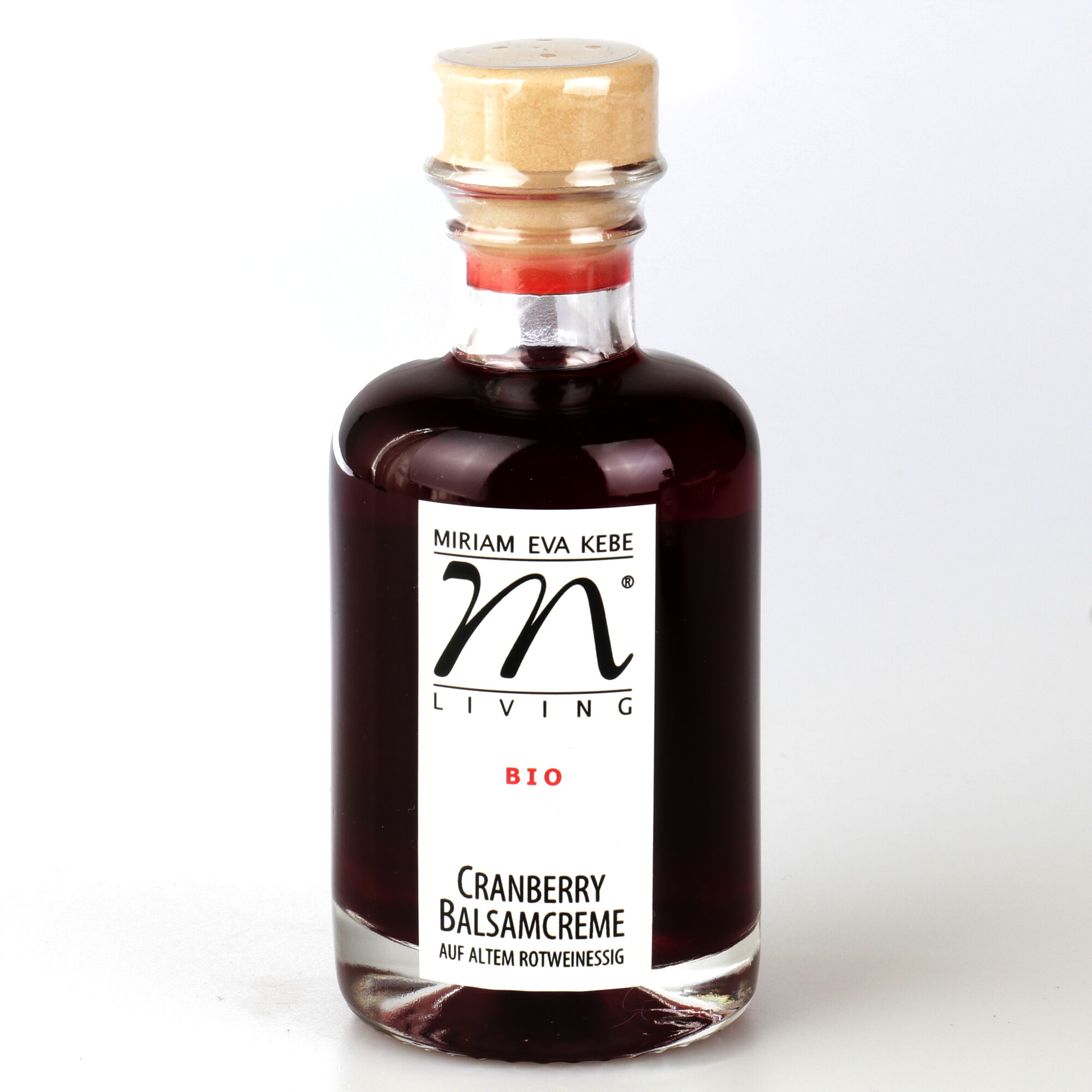 Eine Glasflasche mit dunkler, rotvioletter Cranberry Balsamcreme von Kebe Living. Die Flasche ist mit einem Naturkorken verschlossen und hat ein weißes Etikett mit schwarzer und roter Schrift sowie dem Kebe-Logo. Der Inhalt wirkt dickflüssig und edel.