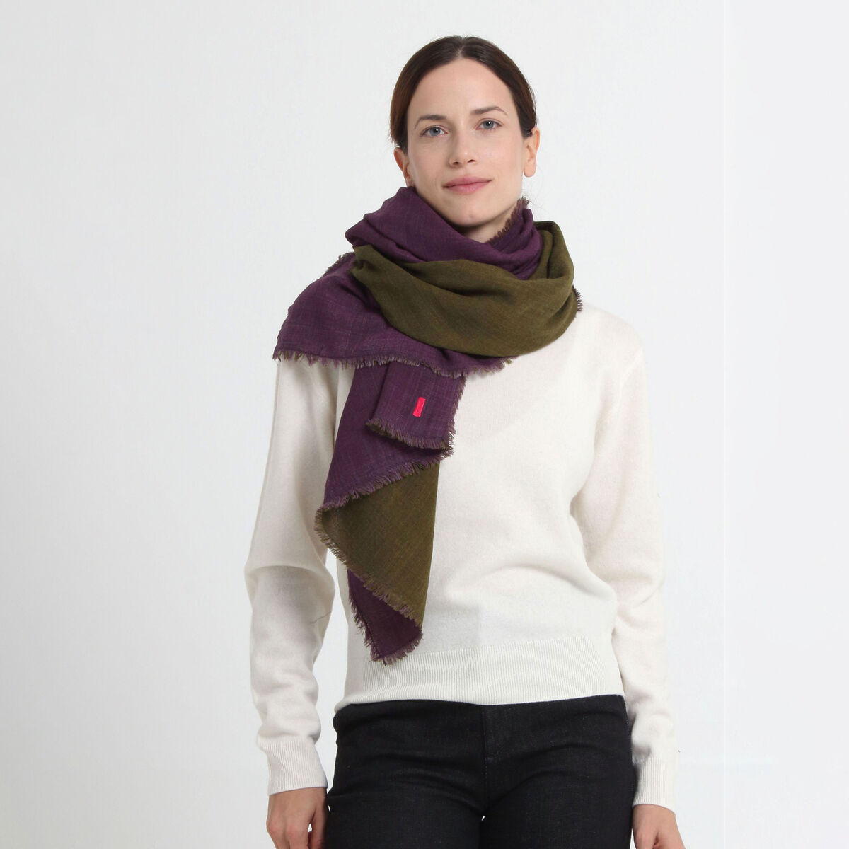 Eine Frau trägt einen großen, weichen Wollschal »Carla« von Shalls Barcelona in Violett und Grün über einem weißen Pullover. Der Schal wirkt angenehm leicht, flauschig und modisch. Er ist elegant drapiert und setzt ein modisches Statement.