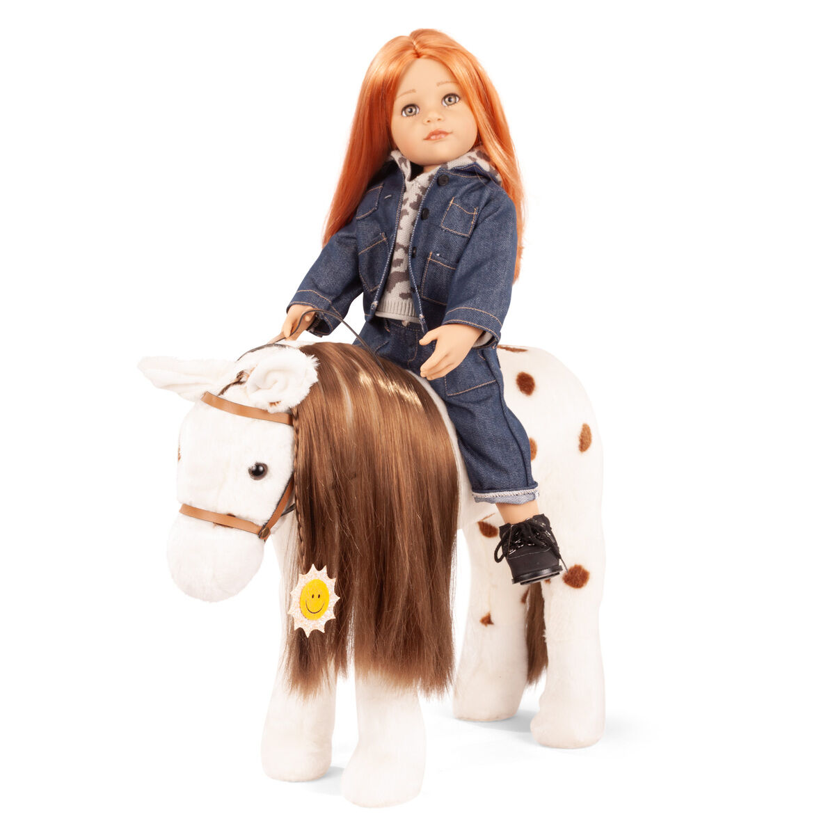 Das Bild zeigt eine Götz Reiterpuppe mit langem, orangefarbenem Haar in Jeans-Outfit auf dem weißen Plüsch-Kämmpferd »Dotty« mit braunen Flecken und langer Mähne. Beide stehen aufrecht, das Pferd trägt ein Zaumzeug. Geeignet für Kinder, detailreich gestaltet.