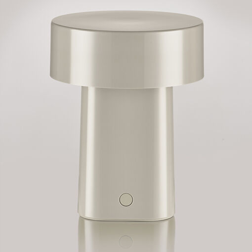 Die Abbildung zeigt eine tragbare, moderne Tischlampe mit minimalistischem Design in cremefarbener Optik. Die Lampe ist zylindrisch und hat oben einen breiten Lampenschirm. Sie steht auf einer glänzenden, reflektierenden Fläche vor einem hellen, neutralen Hintergrund.
