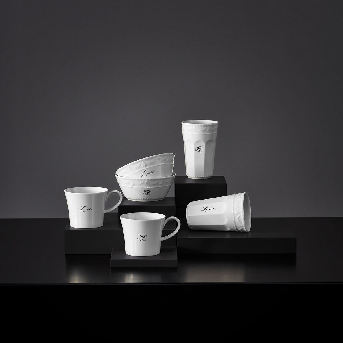 Ein Muesli-Gourmet-Set »Kurland« von KPM aus weißem Porzellan, bestehend aus mehreren stilvollen Schalen und Tassen mit elegantem Design, arrangiert auf schwarzen Podesten.