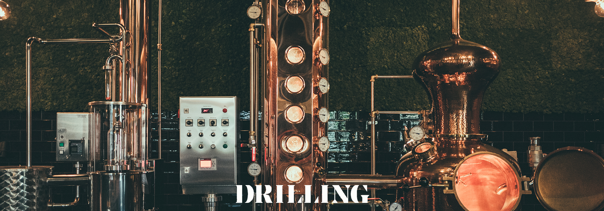 Kupferfarbene Destillationsanlage mit mehreren Kolonnen und Kontrollpaneel in einer Brennerei