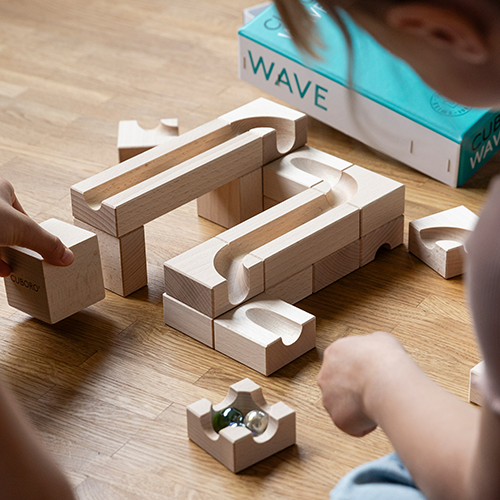 Kinder spielen mit einem Holzbaukasten, der aus gebogenen und geraden Holzteilen sowie Murmeln besteht.