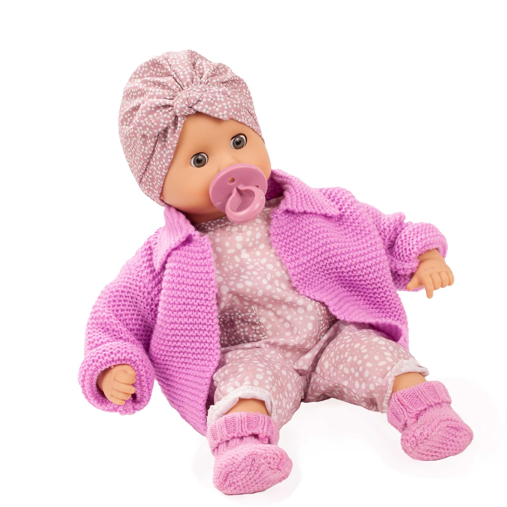 Weiche Babypuppe mit rosa gestricktem Jäckchen, rosa gemustertem Strampler, passendem Stirnband und rosa Socken. Die Puppe sitzt und hält einen Schnuller im Mund. Geeignet als Geschenk für Kinder.