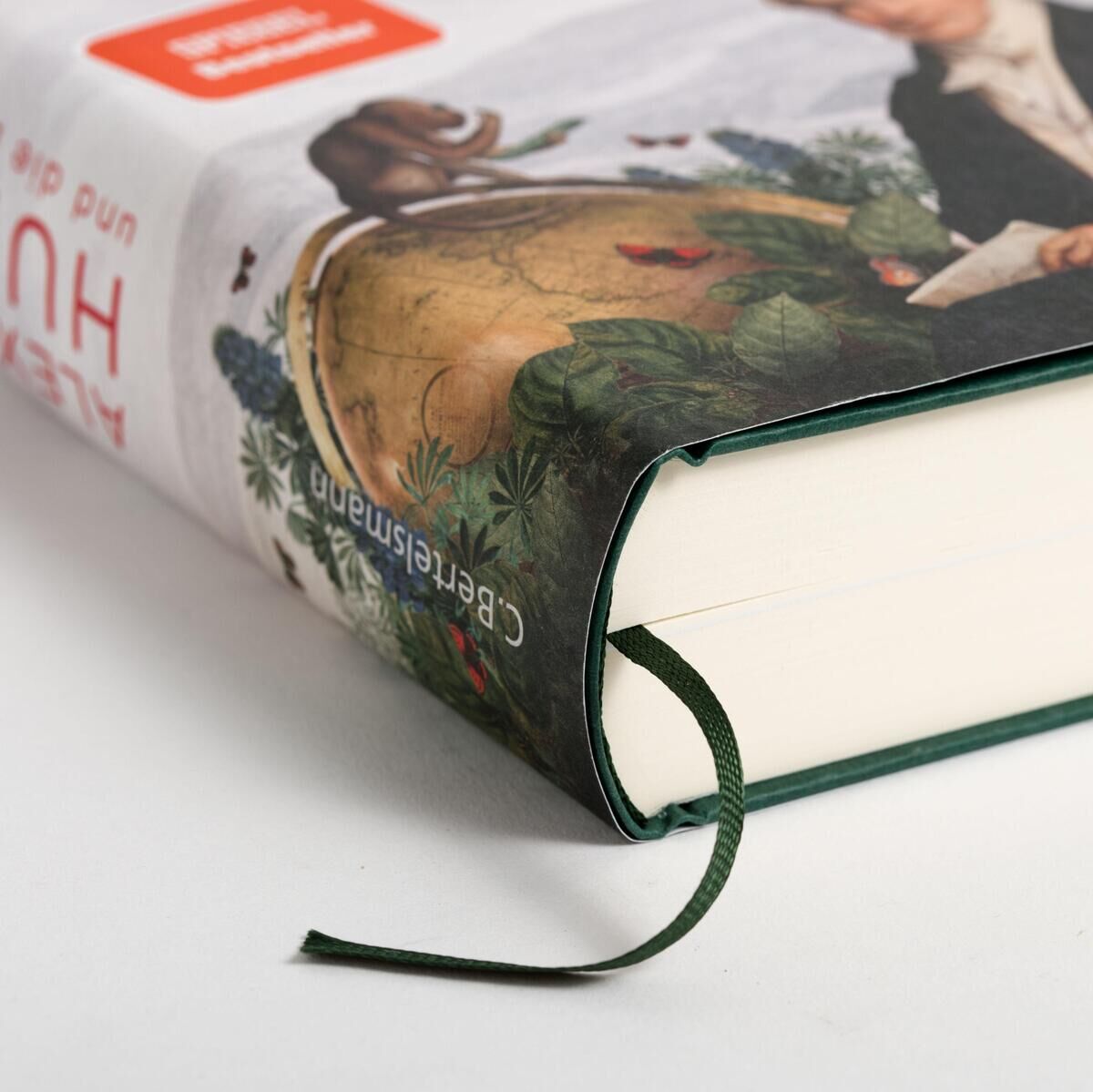 Nahaufnahme des Buches 'Alexander von Humboldt und die Erfindung der Natur' von Wulf. Das Buch ist grün eingebunden mit einem illustrierten Schutzumschlag, der einen Globus und botanische Elemente zeigt.