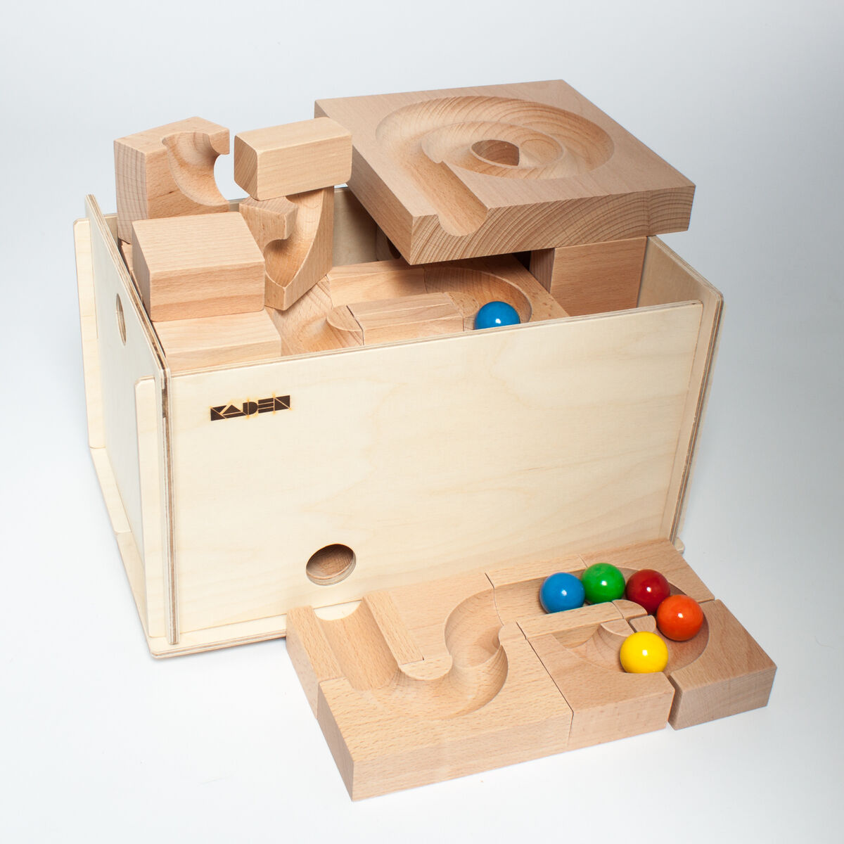 Ein Kugelbahn-Set aus Holz, bestehend aus mehreren Bauklötzen und bunten Kugeln. Die Elemente sind auf einer Holzkiste gestapelt, und die farbigen Kugeln (Rot, Blau, Grün, Gelb) sind auf einem Holzstück angeordnet.