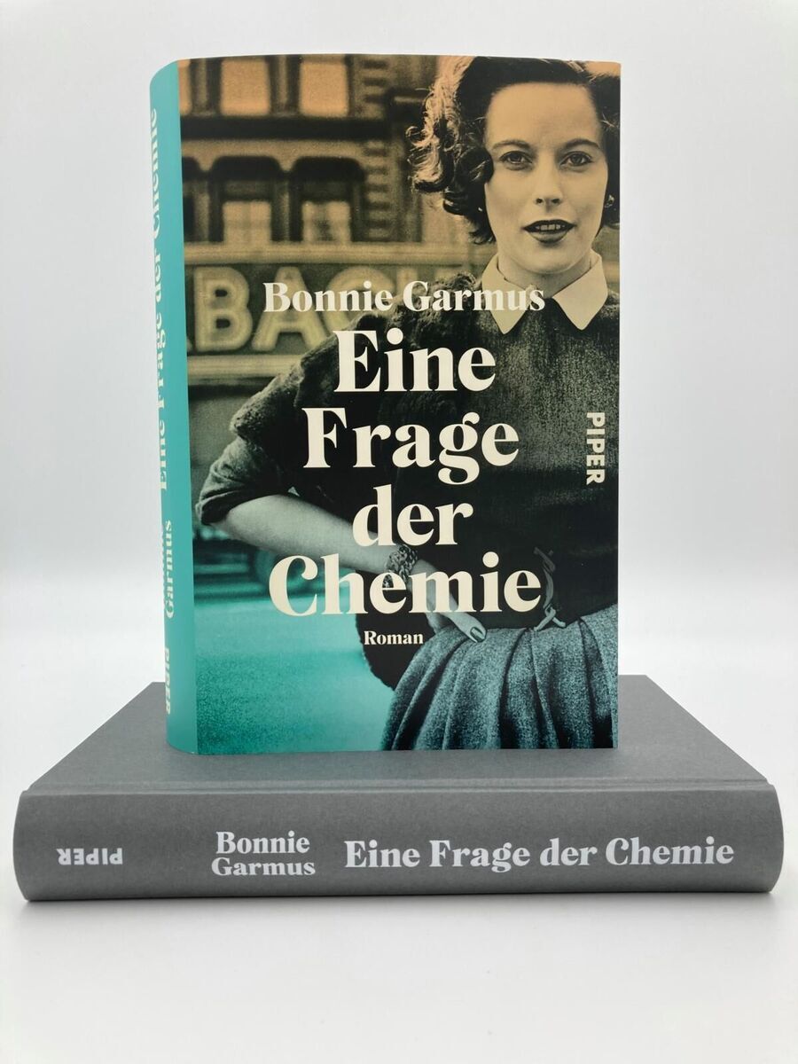 Das Bild zeigt das Buch 'Eine Frage der Chemie' von Bonnie Garmus, veröffentlicht von Piper Verlag. Auf dem Buchumschlag ist eine Frau in Schwarzweiß abgebildet. Das Buch steht auf einer grauen Unterlage, deren Beschriftung ebenfalls 'Bonnie Garmus: Eine Frage der Chemie' lautet.