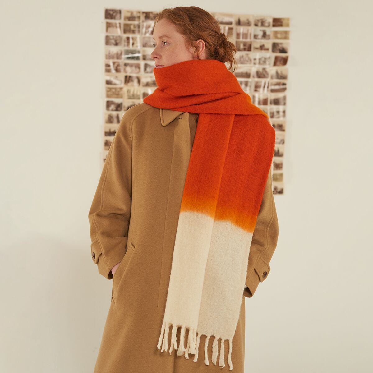 Eine Person trägt einen voluminösen Schal »No.698« von MOISMONT in der Farbvariante tomato. Der Schal besteht aus hochwertiger Schurwolle und Nylon und zeigt einen Farbverlauf von kräftigem Tomatenrot über Orange zu Cremeweiß. Das Accessoire sitzt locker um Hals und Schultern, zu einer beigefarbenen Manteljacke kombiniert.