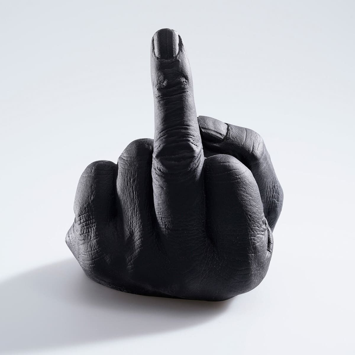 Eine Skulptur von Ai Weiwei mit dem Titel »Study of Perspective in Glass«. Sie zeigt eine realistisch nachgebildete schwarze Hand, die den Mittelfinger hebt. Die Oberfläche der Skulptur ist detailliert und zeigt die Textur der Haut. Die Hand hebt sich stark von dem weißen Hintergrund ab, auf dem sie platziert ist.