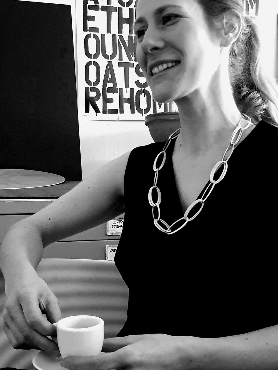 Eine Frau trägt die Halskette „GRACE“ von HML-Collier und hält eine Tasse. Die Kette ist ein modisches, elegantes Accessoire, das die schlichte schwarze Kleidung der Frau ergänzt.